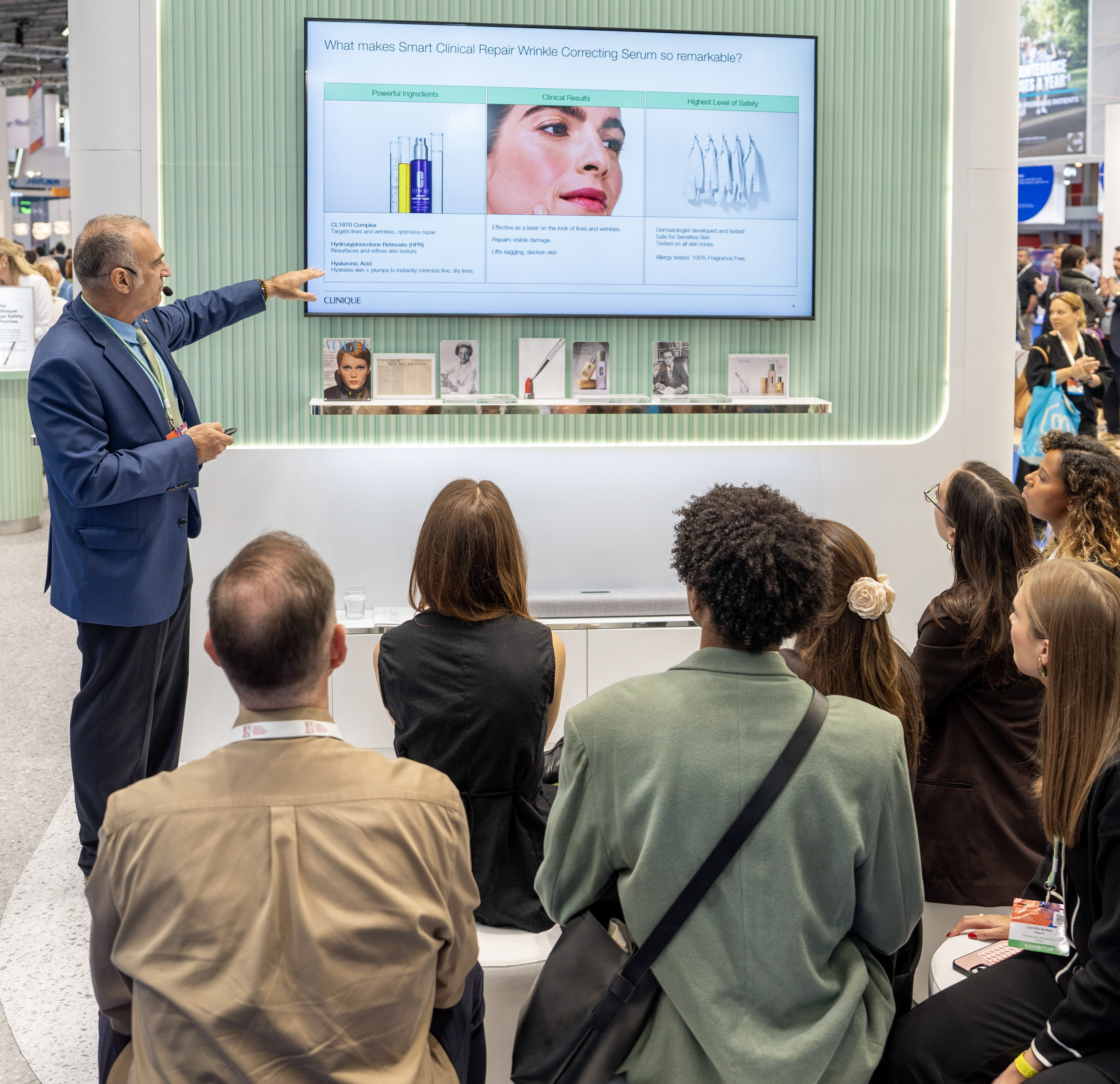 Photo du stand Clinique à l'EADV Amsterdam avec des visiteurs participant à une présentation devant le Dr Tom Mammone